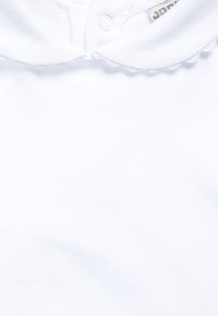 Weißes Baumwollkleidungsstück mit gezacktem Kragen, ausgestattet mit einem Druckknopfverschluss am Ausschnitt und weicher Textur. Schlichtes und unauffälliges Design.
