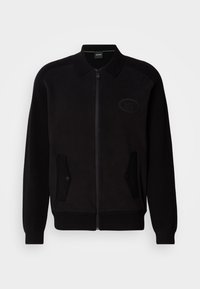 Veste noire zippée avec col, deux poches avant à boutons et logo embossé subtil sur le côté gauche de la poitrine.