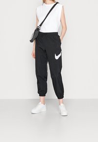 Svarta träningsbyxor med elastisk midja, avsmalnande ärmslut och en vit Nike-logotyp. Parat med en vit ärmlös topp och vita sneakers.