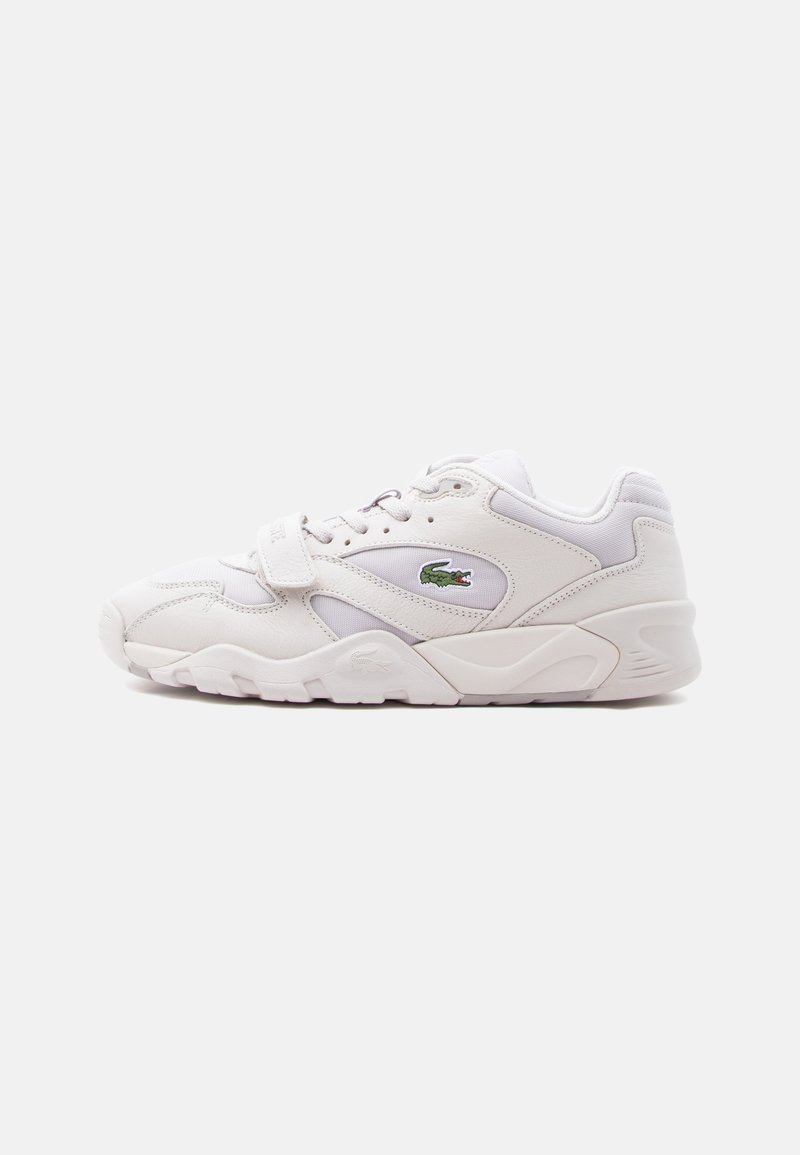 White athletic sneaker with lace and Velcro strap, featuring a green crocodile logo on the side and a thick, textured sole.