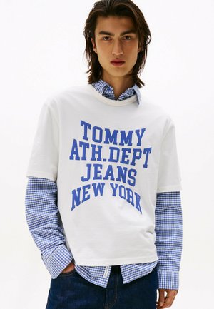 Weißes Baumwoll-T-Shirt mit blauem grafischem Text "TOMMY ATH. DEPT JEANS NEW YORK", über einem blau-weiß karierten Hemd getragen.
