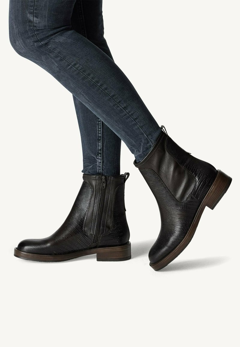 Schwarze Leder-Stiefeletten mit strukturiertem Finish, seitlichen Reißverschlüssen und einem niedrigen, gestapelten Absatz, kombiniert mit dunkelblauen Slim-Fit-Jeans.