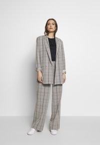 Grau kariertes Anzug mit einem locker sitzenden Blazer und weitem Hosenbein. Darunter ein schwarzes Oberteil und weiße Sneakers. Glatte Stoffoberfläche.