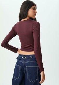 Top fitted a maniche lunghe di colore bordeaux realizzato in tessuto stretch, abbinato a pantaloni in denim scuro a vita alta con due grandi tasche posteriori.