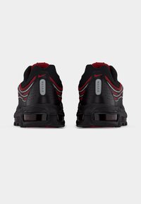 Baskets de sport noires avec accents rouges, tige en mesh et synthétique, amorti Max Air visible et semelle extérieure en caoutchouc avec motif texturé.