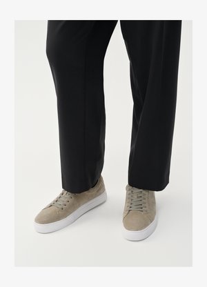 Svetle šedé semišové tenisky s bílou gumovou podrážkou, vybavené kulatými tkaničkami a minimalistickým designem, zkombinované s černými kalhotami.