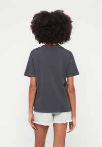 Szürke pamut rövid ujjú póló kerek nyakkivágással és kényelmes szabással, világos farmer rövidnadrággal, amely rojtos szélű.