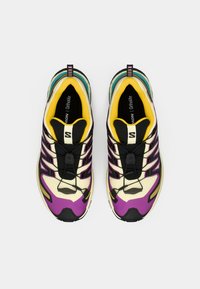 Chaussures de sport multicolores avec un dessus noir et des accents violets, jaunes et turquoises. Semelle texturée et système de laçage présents.