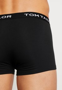 Schwarze Baumwoll-Boxershorts mit breitem elastischem Bund, auf dem der Markenname "TOM TAILOR" in weißen Buchstaben zu sehen ist. Glatte Textur, körpernahe Passform.