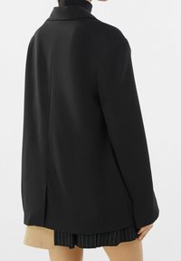 Svart kavaj med klassisk krage, skräddarsydd passform och mjukt tyg. Bakdelen har en mittsöm och minimal detaljering.