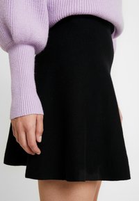 Zwarte vloeiende rok met een zachte textuur, gepresenteerd naast een lavendelkleurige gebreide trui. De rok heeft een schone zoom en minimale details.
