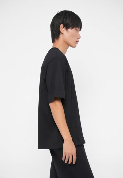 Črna bombažna majica s sproščenim krojem, kratkimi rokavi in zaobljenim izrezom. Gladka tekstura, minimalističen design, nosi se z usklajenimi hlačami.