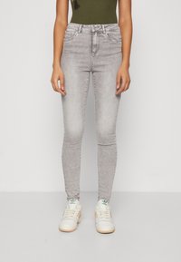 Jeans skinny de tiro alto en gris, con una textura desgastada y diseño clásico de cinco bolsillos, combinados con zapatillas blancas con detalles en verde.