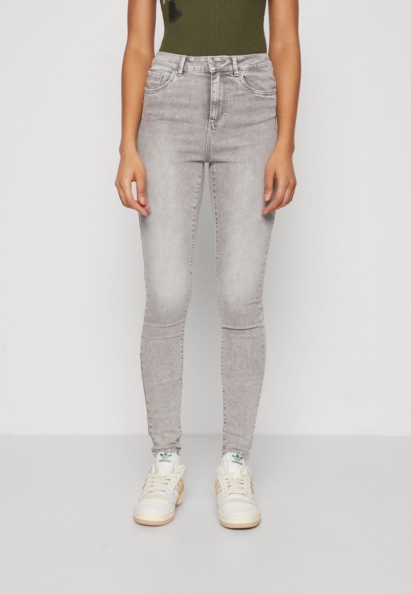 Jeans skinny de tiro alto en gris, con una textura desgastada y diseño clásico de cinco bolsillos, combinados con zapatillas blancas con detalles en verde.
