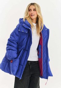 Modrý péřový kabát s kapucí, zdobený diagonální prošívanou texturou, s patentními knoflíky a zipem na zapínání a kontrastní fialovou podšívkou.