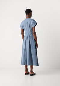 Lichtblauw, jurk met cap sleeves en A-lijn, met een knoop in de taille. Soepele textuur, halverwege de kuit, gedragen met zwarte blokhak sandalen.