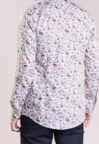 Camicia a maniche lunghe in tessuto leggero con un motivo stampato di animali colorati su uno sfondo chiaro, con polsini abbottonati e orlo curvo.