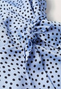 Tissu bleu clair à pois noirs noué en un nœud décoratif, présentant une texture lisse et légèrement brillante.