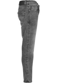 Jeans de mezclilla gris con corte ajustado, textura deslavada, diseño de cinco bolsillos y cinturilla con marca. La pierna se estrecha en el tobillo.