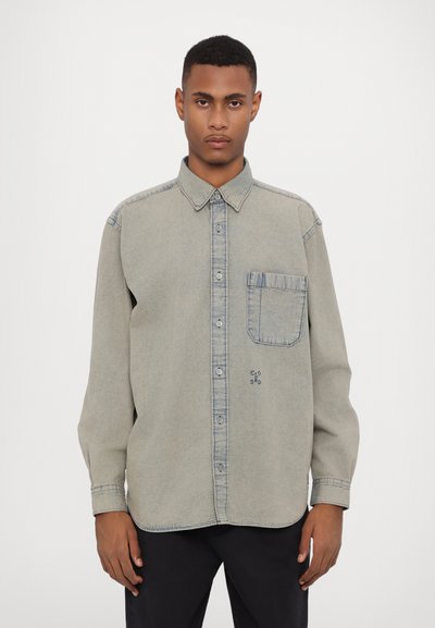 Lichtgrijze button-up shirt met een kraag, een enkele borstzak en blauwe stiksels. Heeft een relaxed fit en lange mouwen.