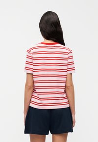 Κόκ κινη και λευκή ριγέ μπλούζα με στρογγυλή λαιμόκοψη, κοντά μανίκια και άνετη εφαρμογή. Φορεμένη με σκούρα μπλε σορτς.