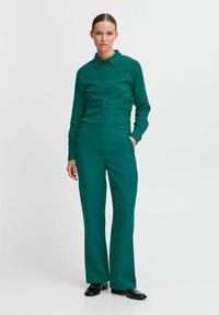 Completo su misura color turchese con camicia a colletto e pantaloni a gamba larga, realizzato in tessuto liscio con un design pulito e strutturato.