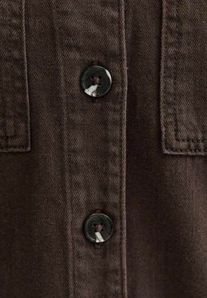 Close-up van bruin stof met twee gemarmerde donkere knopen, vastgenaaid met bijpassend garen, met gedetailleerd stikwerk en een gestructureerd materiaal.