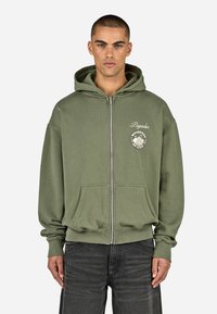 Olíva zöld cipzáras kapucnis pulcsi, pamutból készült, elülső zsebbel, bordás mandzsettákkal és logónyomattal a bal mellen.