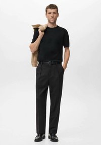 Cămașă neagră cu mânecă scurtă, pantaloni gri închis, curea neagră și pantofi negri. Sacou bej aruncat pe umăr. Design simplu, croit.