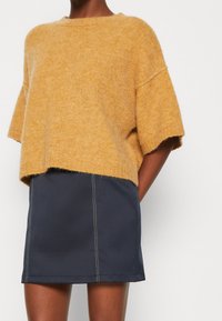 SENAPSGUL, kortärmad stickad tröja med avslappnad passform, parat med en mörkblå kjol med vita stygn detaljer.