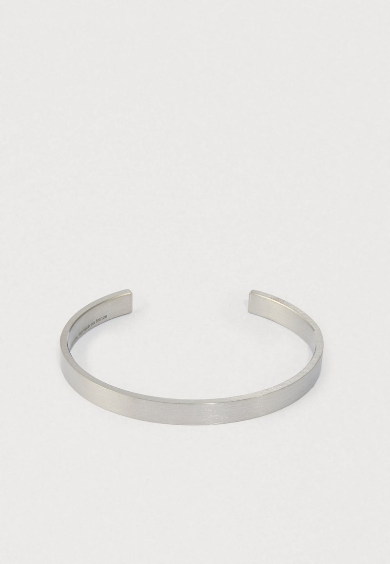 Bracciale in metallo argentato aperto con una finitura spazzolata su uno sfondo neutro.