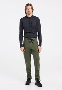 Čierny termálny dlhý rukáv s polovičným zipsom a náprsníkovou vreckom, spárovaný so zelenými nohavicami s elastickým pásom a čiernymi topánkami.