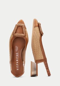 Zapatos de tacón cuadrado de cuero marrón y paja trenzada, con un detalle de hebilla cuadrada estructurada en la punta y un diseño lateral texturizado.