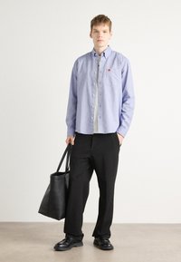 Lyseblå skjorte med knapper og brystlomme, parret med svarte bukser og en svart totebag. Glatt stoff, avslappet passform, minimal design.