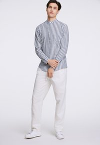 Gestreepte lange mouwen shirt in blauw en wit katoen met een mandarijnkraag, gecombineerd met witte linnen broek en witte sneakers.