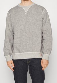 Gray sweatshirt made of cotton blend fabric, featuring ribbed cuffs and hem, round neck, and a small logo tag on the lower hem.