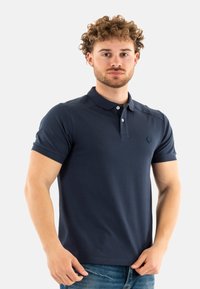 Polo de color azul marino hecho de una tela suave y texturizada; presenta un collar clásico, una tapeta de dos botones y un logotipo en el pecho.