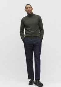 Donkergroen coltrui, slim-fit marineblauwe broek en zwarte instapschoenen. Glad textuur, op maat gemaakt ontwerp, staand tegen een effen achtergrond.