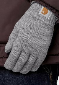 Guante de punto gris con puño acanalado, con un pequeño parche de logo naranja. El guante se lleva en una mano sobre un fondo oscuro.