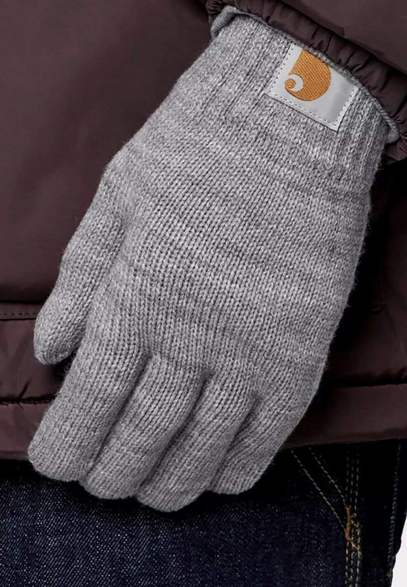 Guante de punto gris con puño acanalado, con un pequeño parche de logo naranja. El guante se lleva en una mano sobre un fondo oscuro.