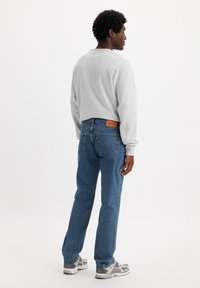 Sudadera gris con cuello redondo, jeans de mezclilla azul con un parche de cuero y zapatillas grises con acentos reflectantes.
