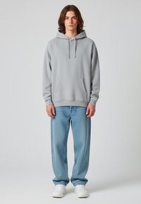 Felpa grigia in cotone con tasca frontale e cappuccio con cordino, abbinata a jeans dritti azzurri e sneakers bianche.