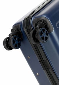 Valigia rigida navy con ruote nere, chiusura a zip e rivetti metallici. Le ruote hanno un design a cinque razze per garantire stabilità.
