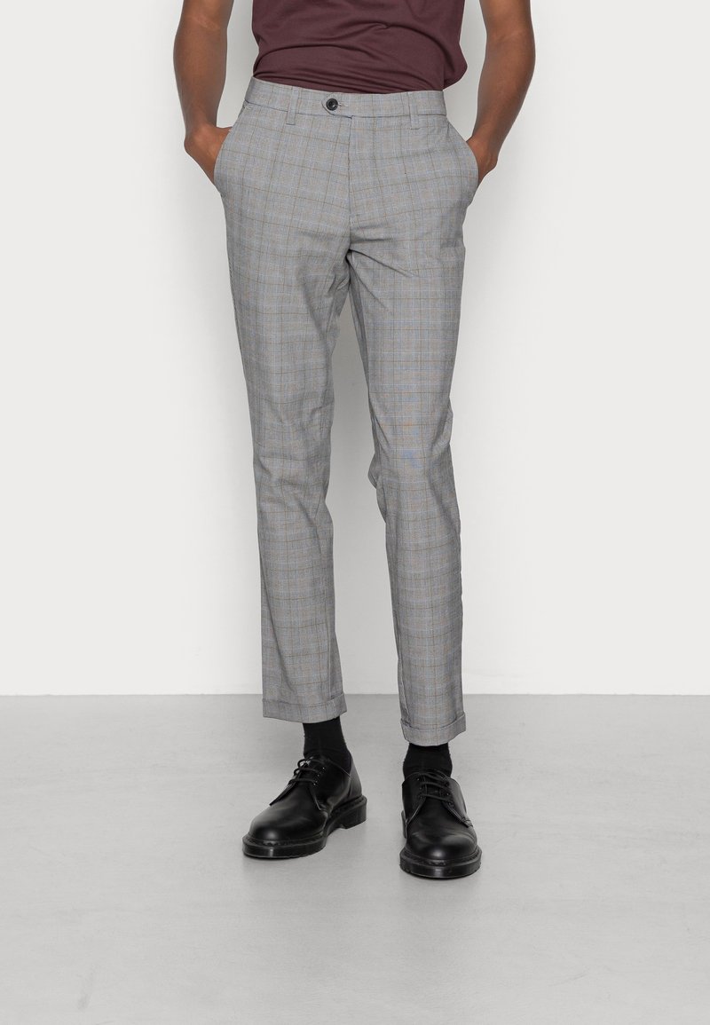 Pantaloni a quadri grigi con vestibilità slim, dotati di chiusura con bottoni e tasche. Indossati con scarpe nere e calze per un look completo.