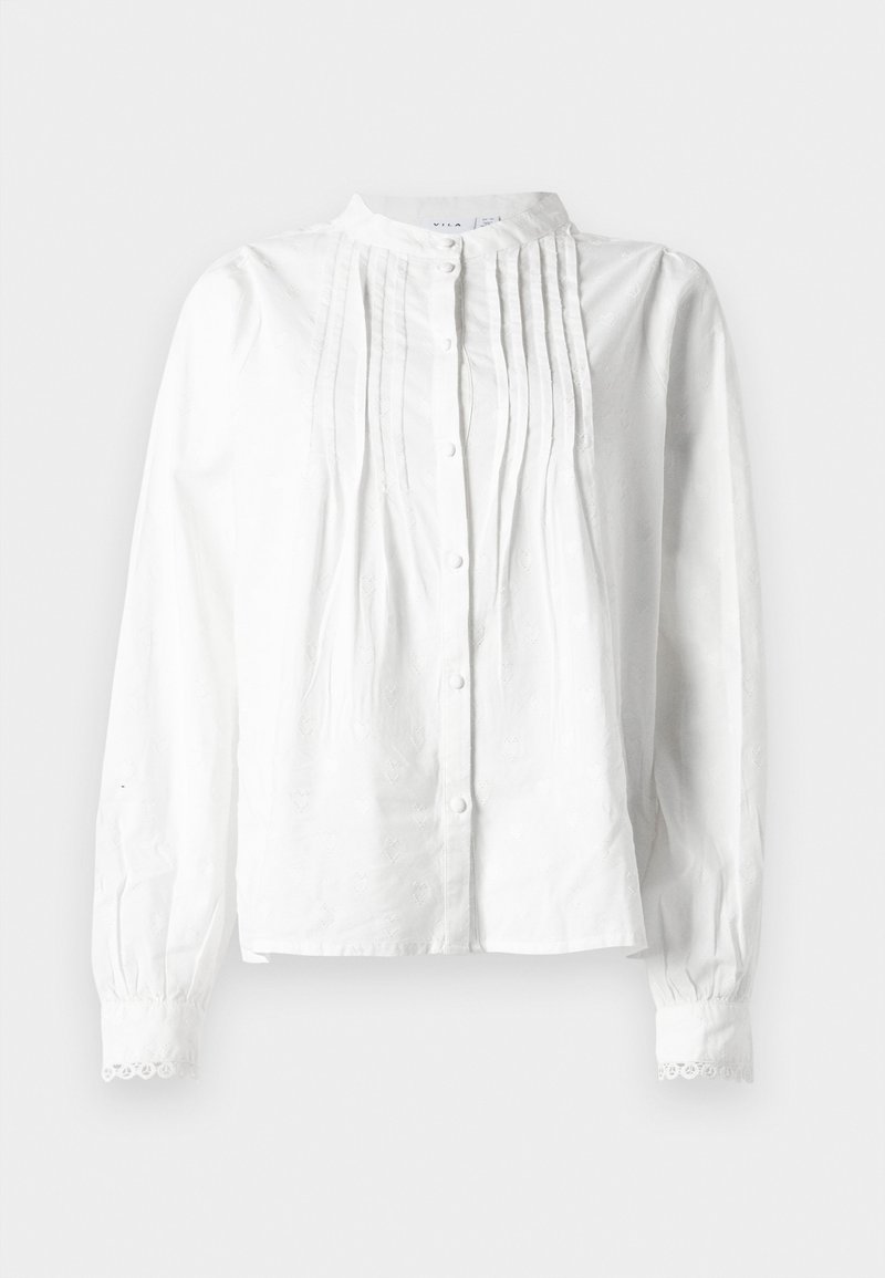 Blouse blanche à manches longues avec col montant, plis verticaux à l'avant, fermeture à boutons et poignets bordés de dentelle.