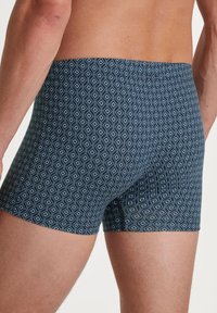 Blauwe geblokte boxershorts van zachte stof, met een geometrisch ontwerp met lichtblauwe diamanten op een marineblauwe achtergrond.