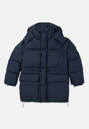 Navy puffer jacket with a high collar, two large front pockets, and a branded patch. Features a drawstring hem and snap closures.