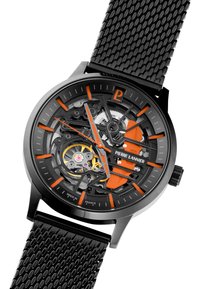 Mechanisk ur med sort meshrem, sort skeleton urskive, orange accenter og sølv hardware. Indeholder eksponerede gear og et logo.