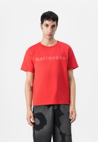 Červené bavlněné tričko s kulatým výstřihem a nápisem "marimekko" v světle šedém potisku na hrudi. Jednoduchý design.