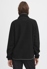 Must musta pullover kõrge kaelusega, pikad varrukad, elastsete mansettidega ja kontrastse halli äärega, valmistatud pehmest ja tekstuurist materjalist.